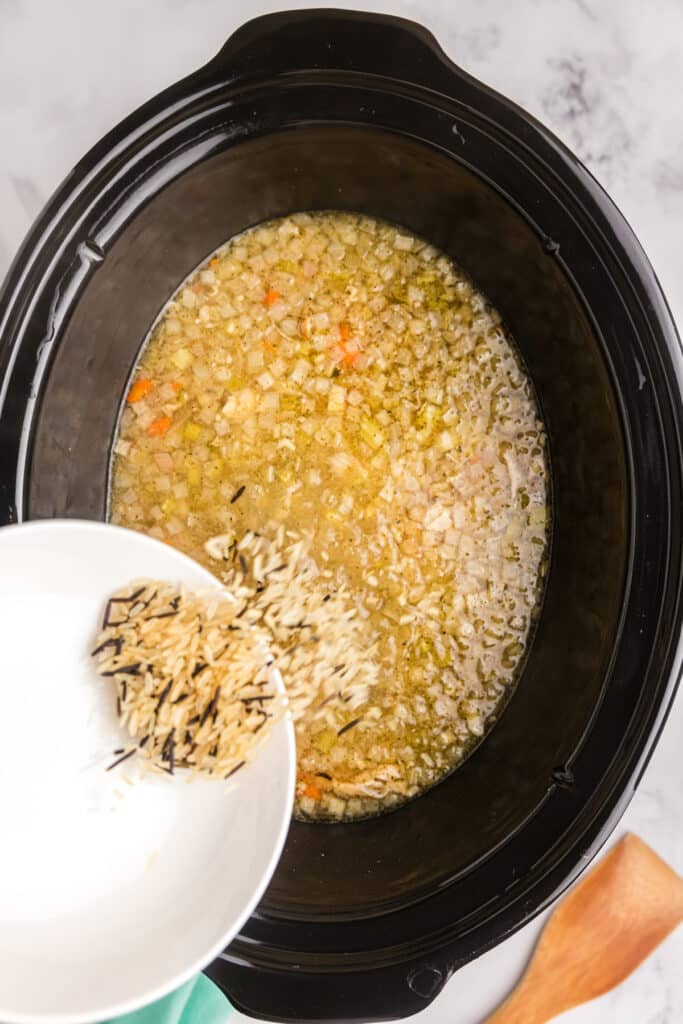 wild rice pouring into a crockpot of soup.