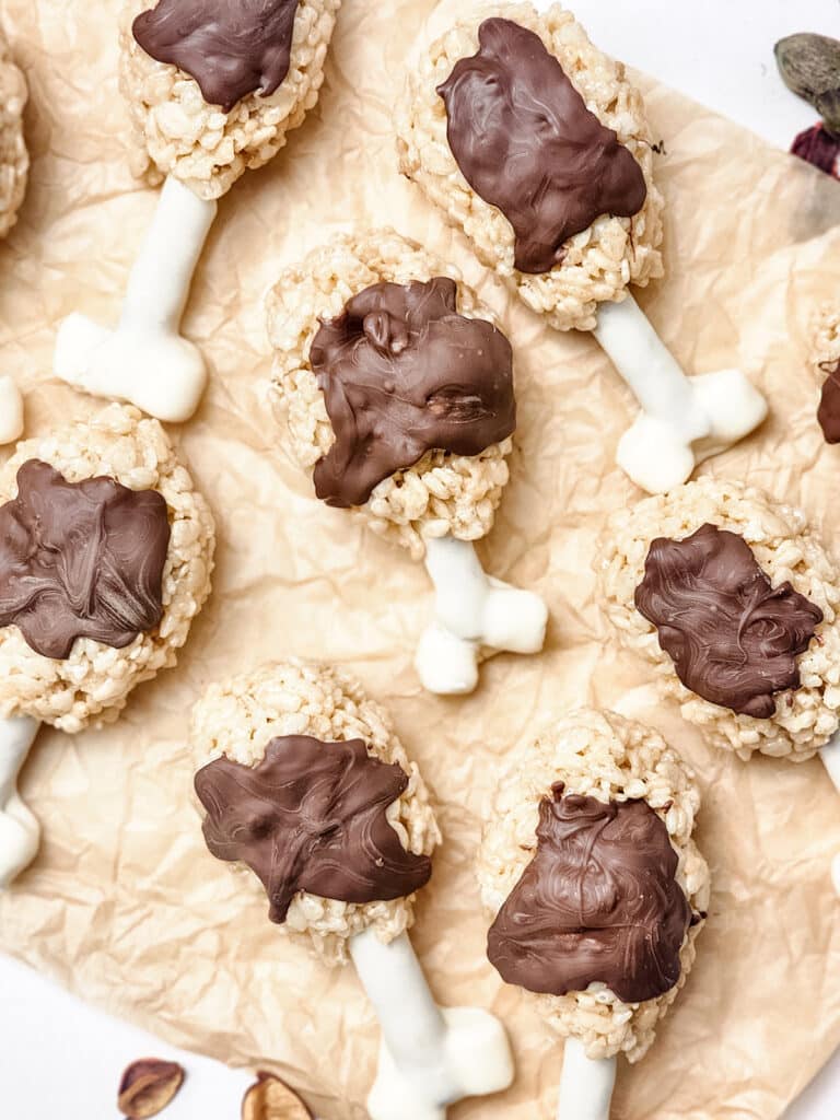 Rice Krispies treats shaped like turkey legs with white candy bones drizzled with chocolate on parchment paper.