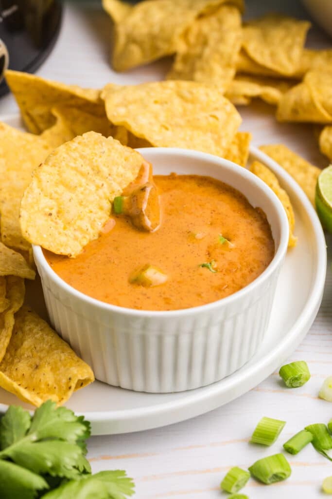 A small ramekin of queso dip with tortilla chips on the side.