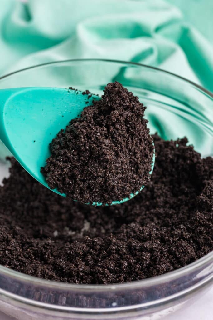 Mixing Oreo crumbs and butter with a teal spatula.