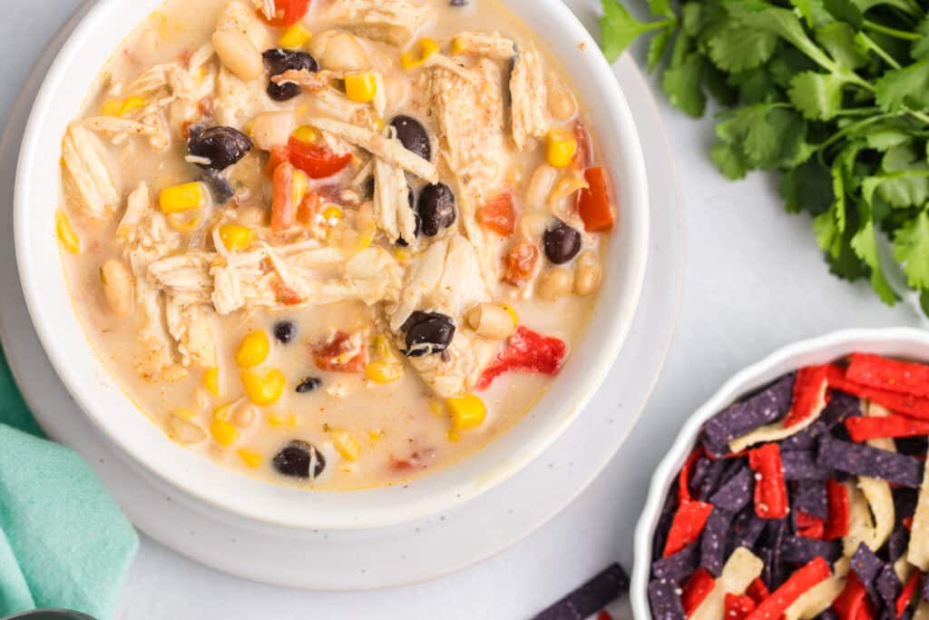 overhead shot of a bowl of creamy tortilla soup next to a bowl of colorful tortilla strips.