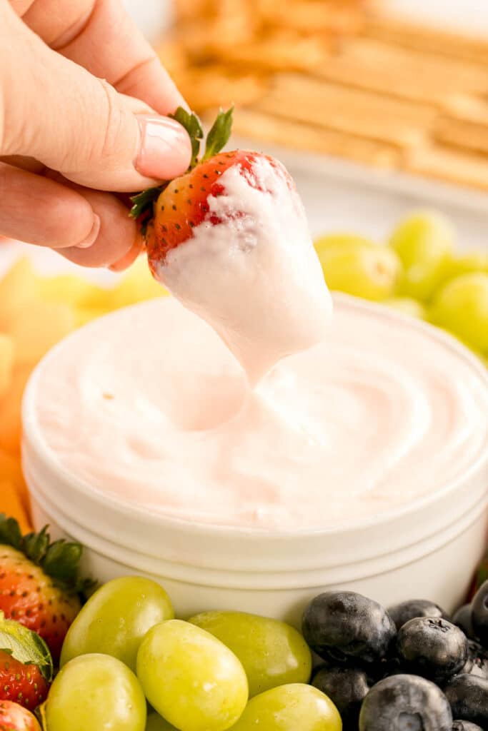 hand dipping a strawberry into fruit dip.