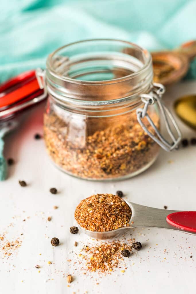 An open jar of Montreal steak seasoning with a measuring spoon filled with the spice mix.