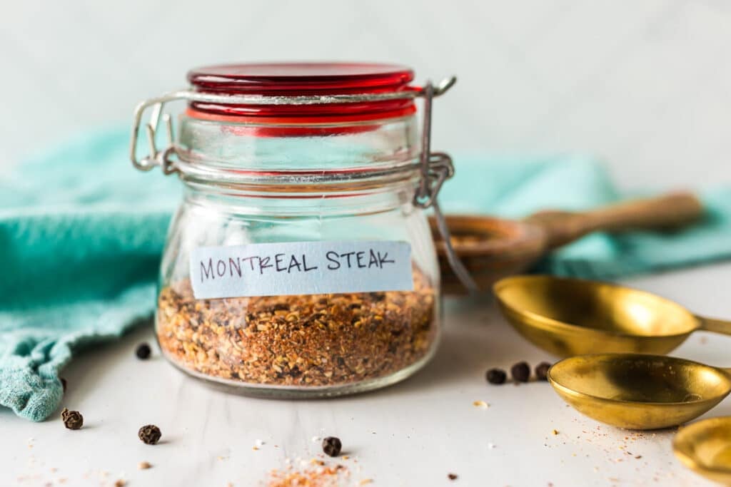 A glass jar with a red lid labeled "Montreal Steak" filled with homemade seasoning.