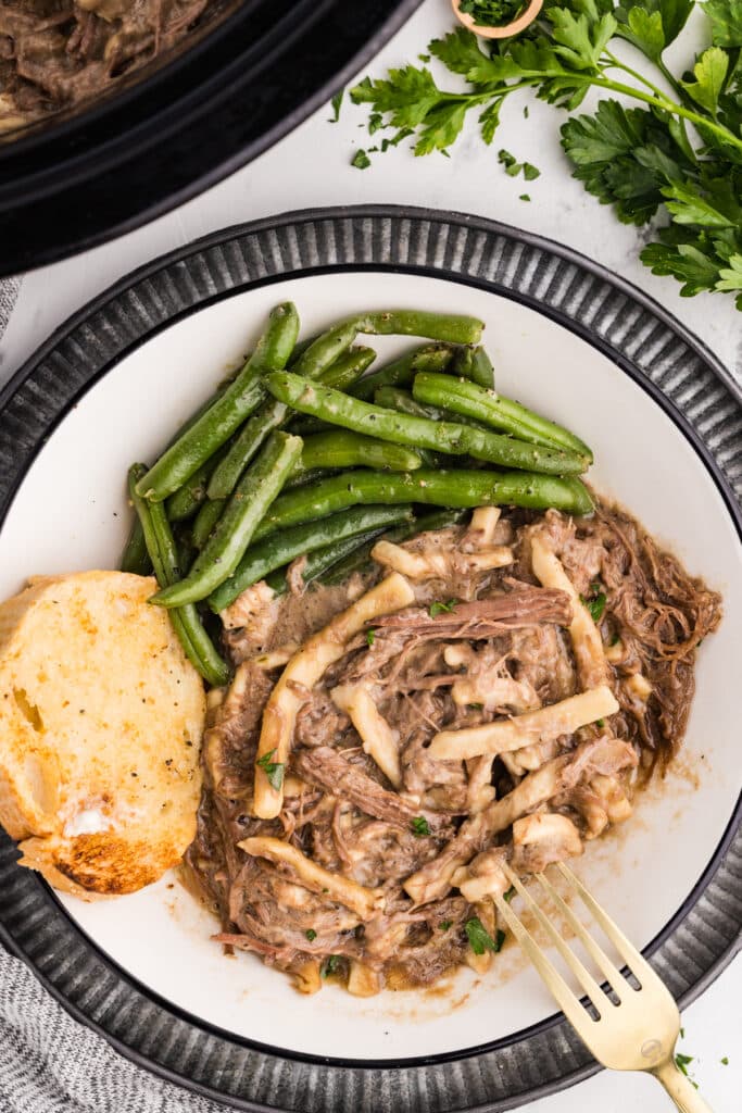 plate of beef and noodles with green beans and garlic bread.