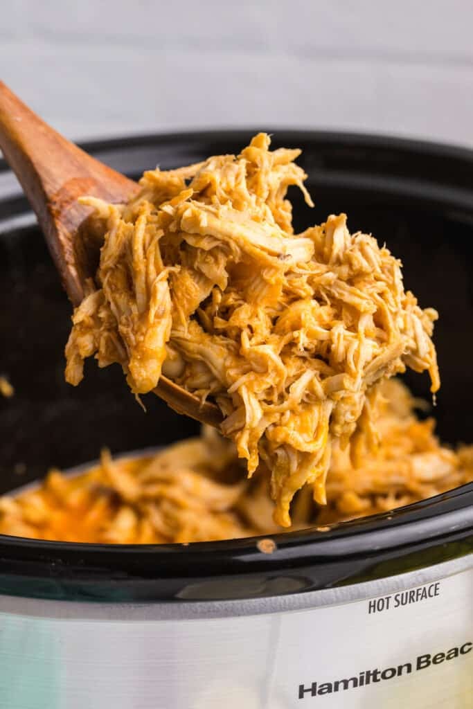 scoop of shredded nashville hot chicken being lifted from a crockpot.