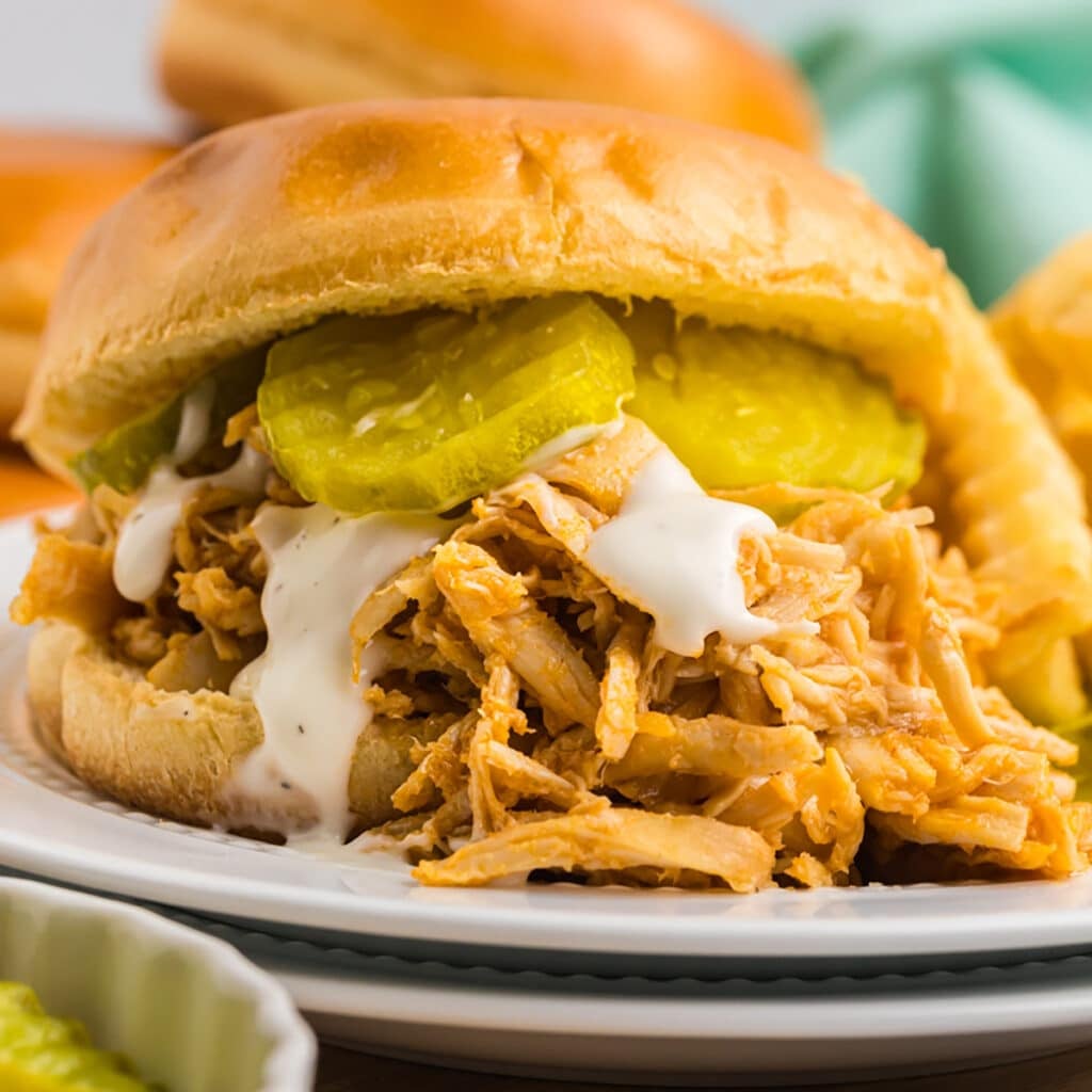 shredded chicken sandwich with pickles and ranch on a brioche bun.