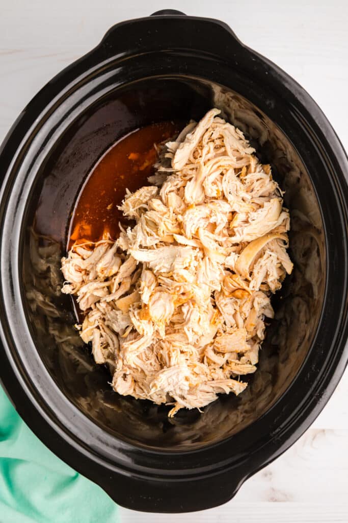 shredded chicken in a slow cooker filled with sauce.