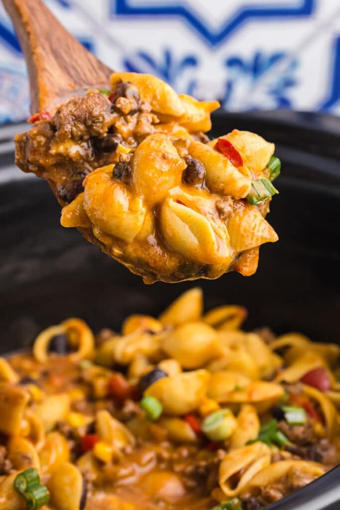 wooden spoon lifting a scoop of taco pasta from a slow cooker.