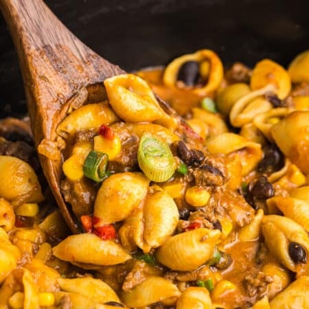 wooden spoon scooping taco pasta from a crockpot.
