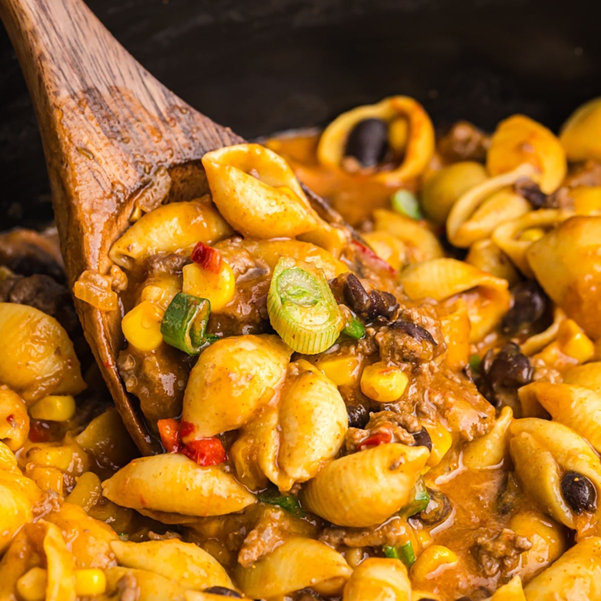 wooden spoon scooping taco pasta from a crockpot.