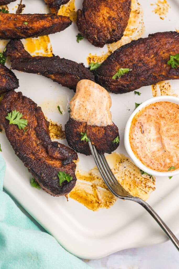 A plate of blackened chicken tenders a bite on a fork.