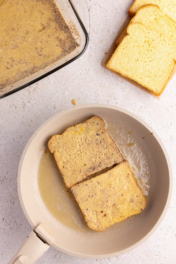 Two slices of brioche bread cooking in a pan coated with melted butter.