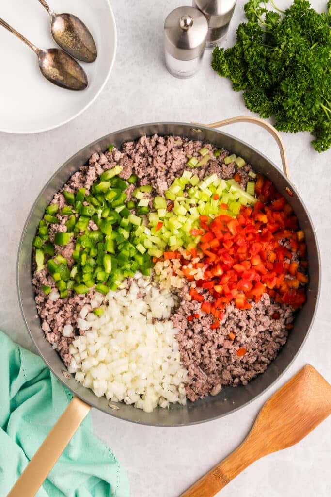 Chopped vegetables on top of cooked ground meat in a skillet.
