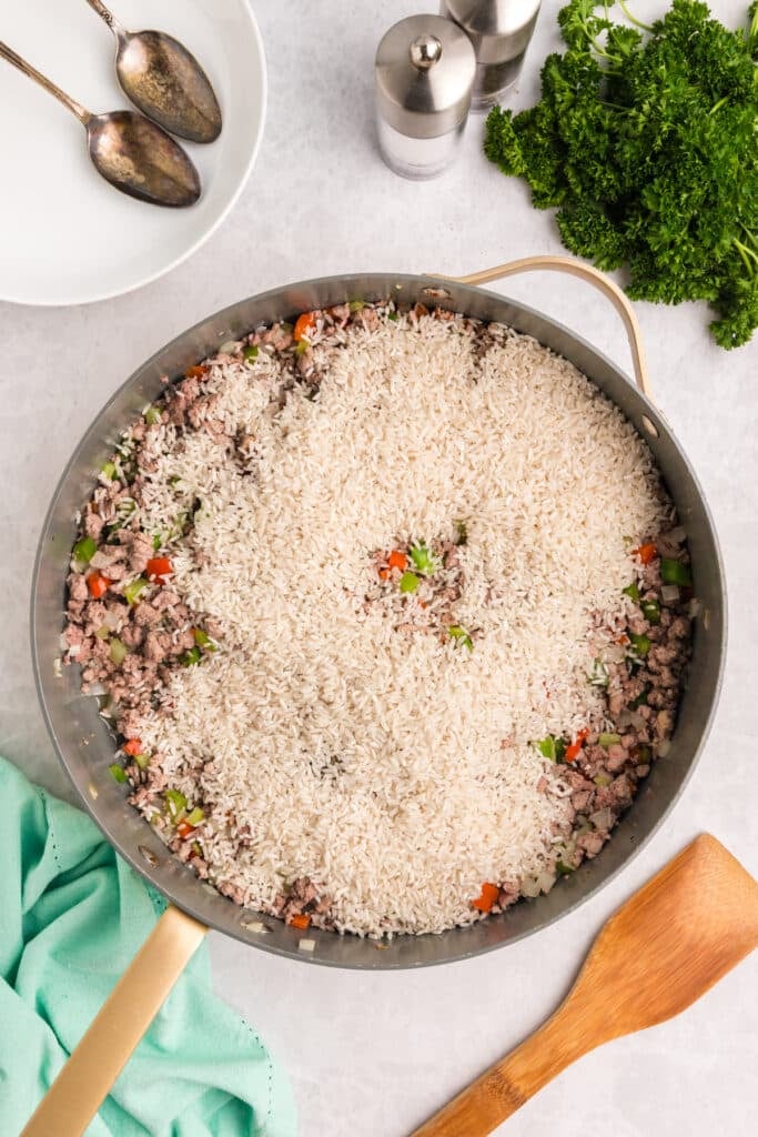 White rice added to a skillet of meat and vegetables.