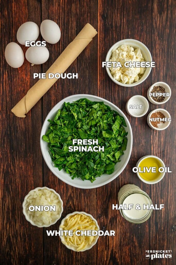 Ingredients for spinach feta quiche arranged on a wooden surface, each labeled.