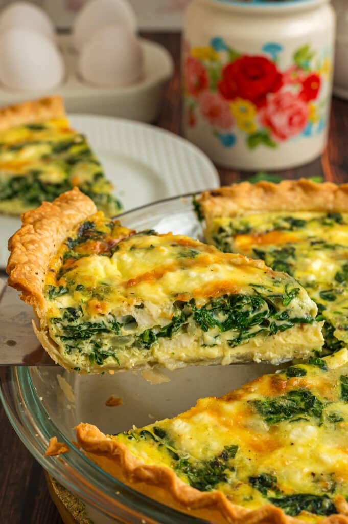 A slice of spinach and feta quiche being lifted from the pie dish, showing the creamy, cheesy layers inside.