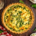 A golden-brown quiche with visible spinach and melted cheese in a flaky pie crust, shot from overhead.