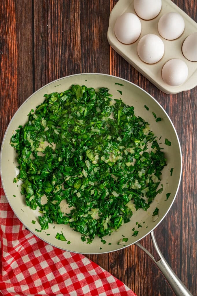 A skillet filled with chopped spinach and onions being sautéed.