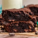 Stack of two thick, fudgy brownies with melty chocolate chunks on a wooden surface.