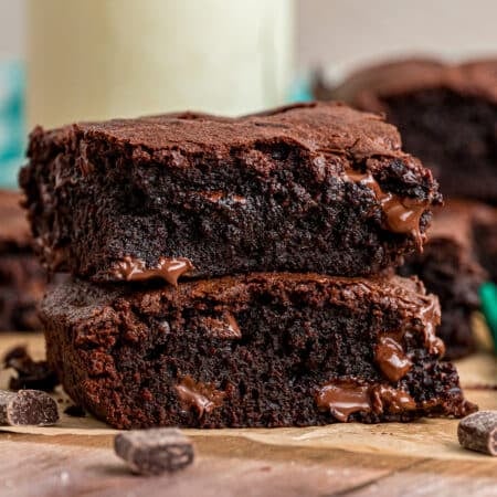 Stack of two thick, fudgy brownies with melty chocolate chunks on a wooden surface.