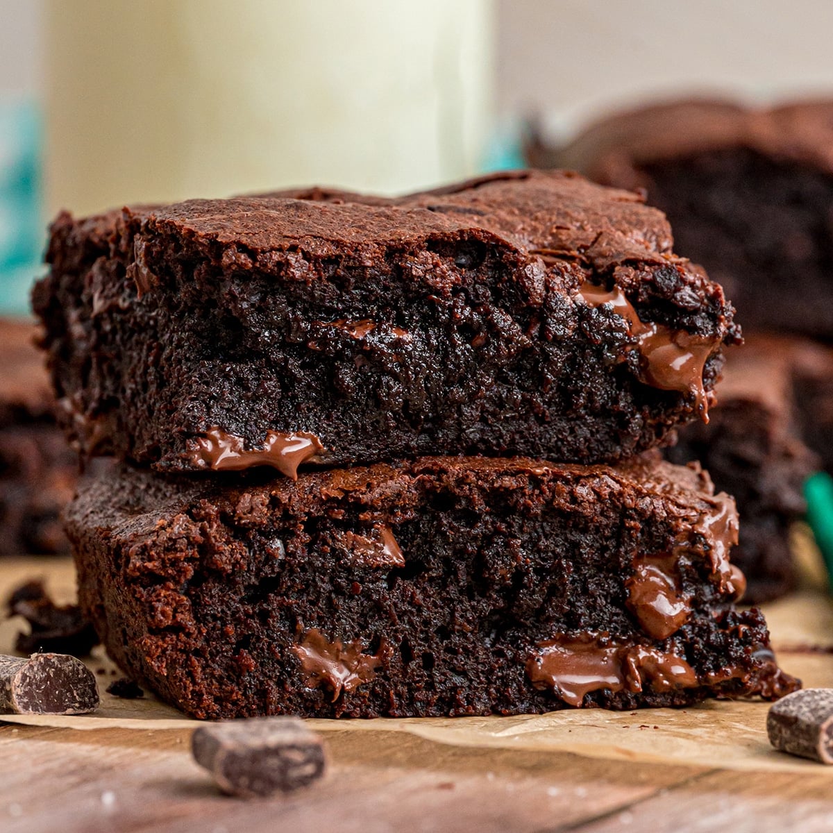 Stack of two thick, fudgy brownies with melty chocolate chunks on a wooden surface.