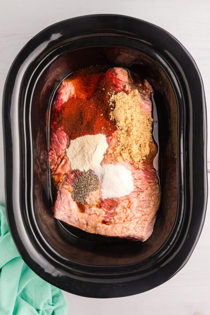 Raw brisket in a slow cooker topped with dry seasonings.