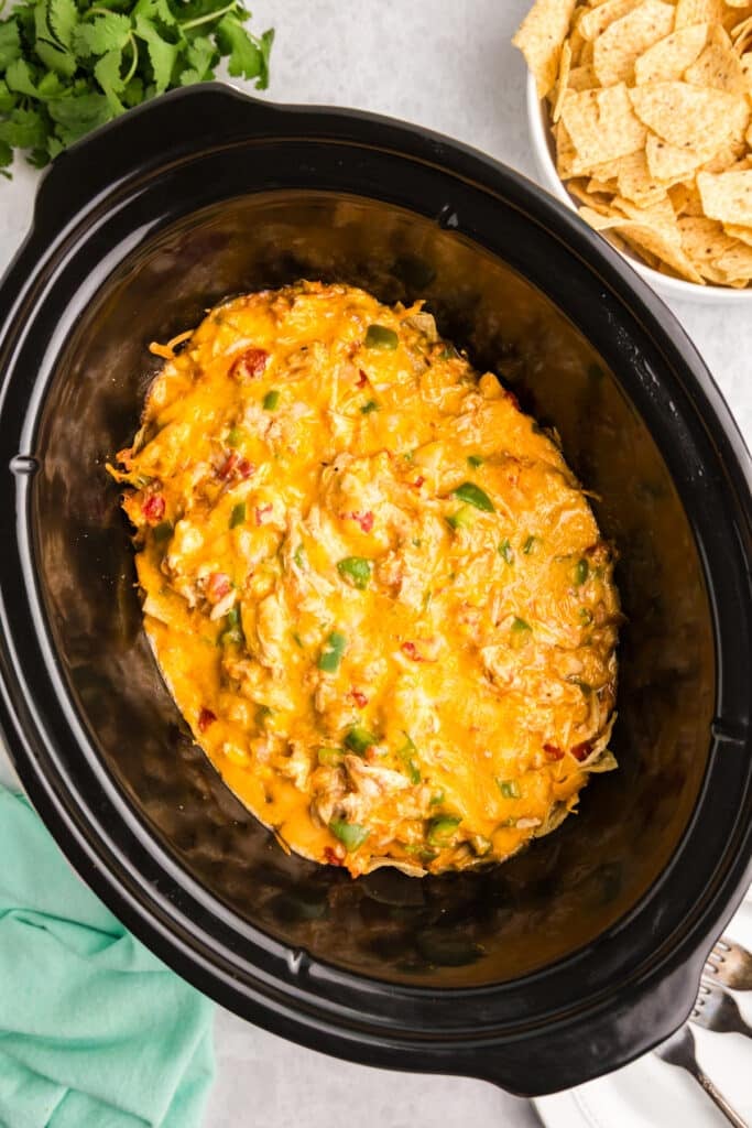 A black slow cooker filled with a baked King Ranch chicken casserole.