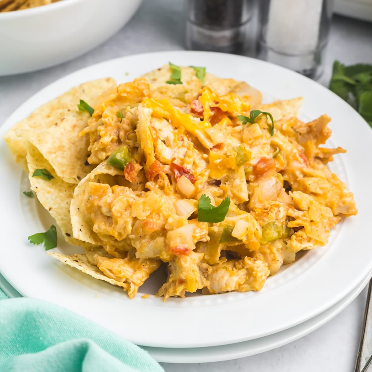 A white plate is piled with crock pot King Ranch chicken over tortilla chips.