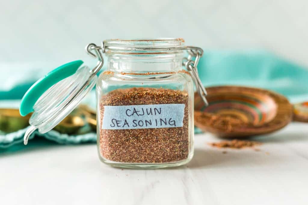 Glass jar labeled “Cajun Seasoning” on a white surface with an open lid.
