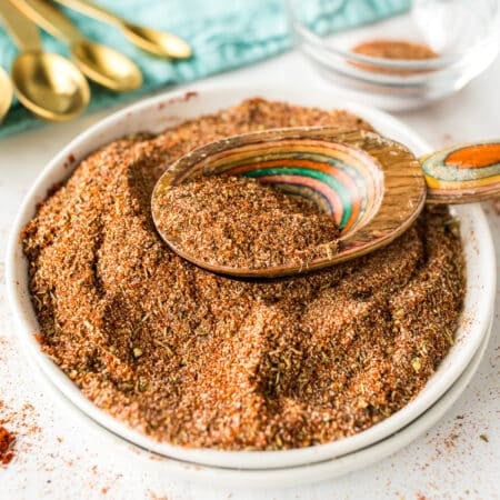 Wooden spoon scooping Cajun seasoning from a full white bowl.