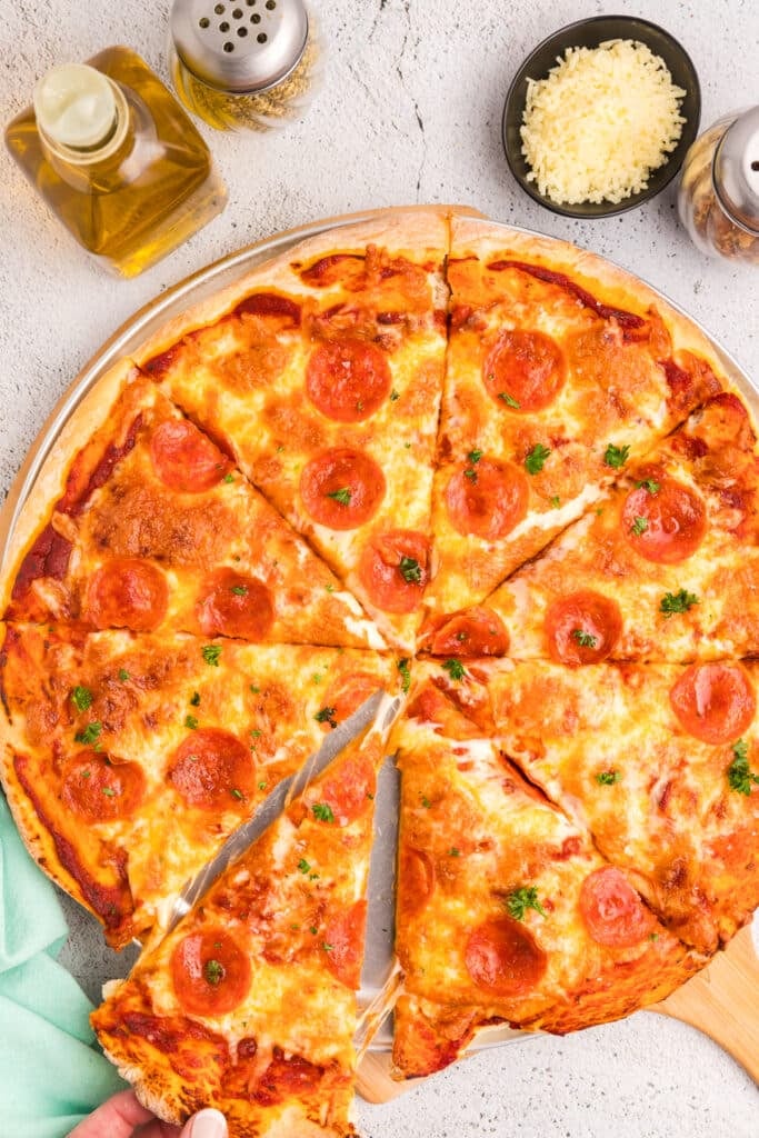 Cooked pepperoni pizza sliced into pieces on a tray, with condiments and cheese bowl around it.