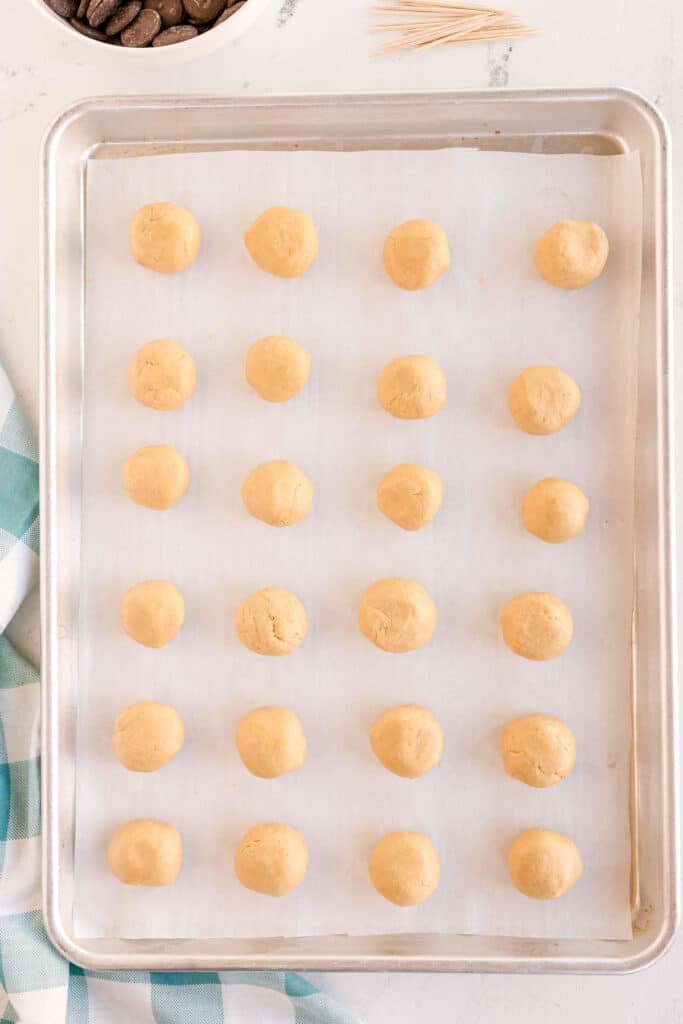 Peanut butter balls lined on a baking sheet.