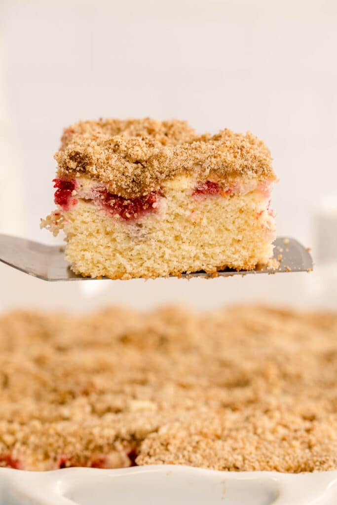 A square of raspberry coffee cake on a spatula held above the baking dish.