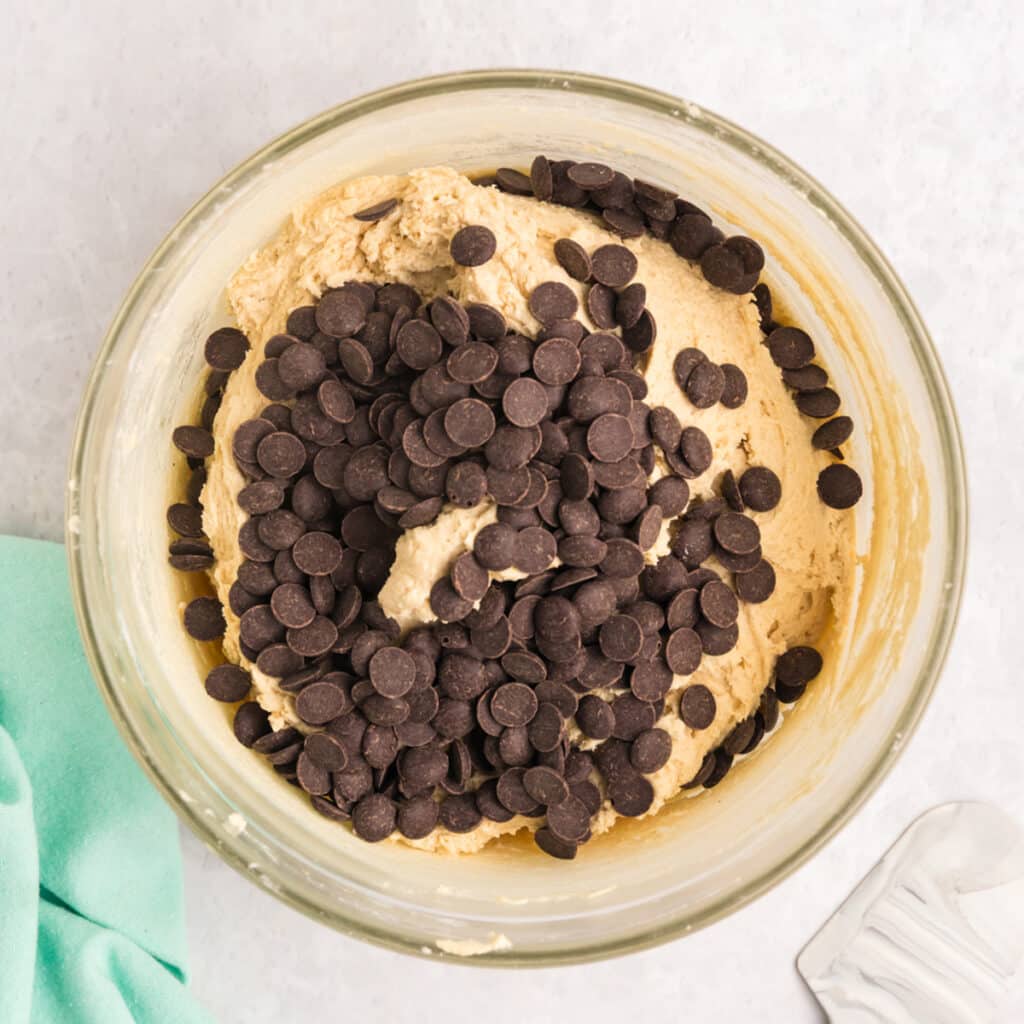 A mixing bowl filled with chocolate chip cookie dough topped with a generous pile of chocolate chips.