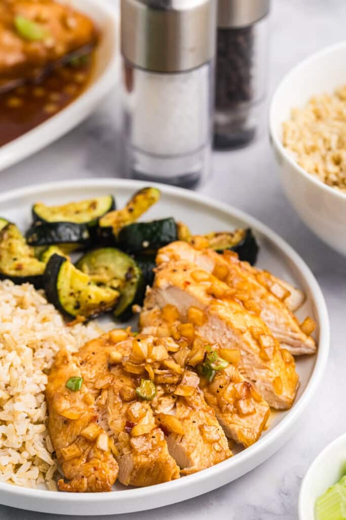 Plated honey bourbon chicken with zucchini and rice, salt and pepper shakers behind.
