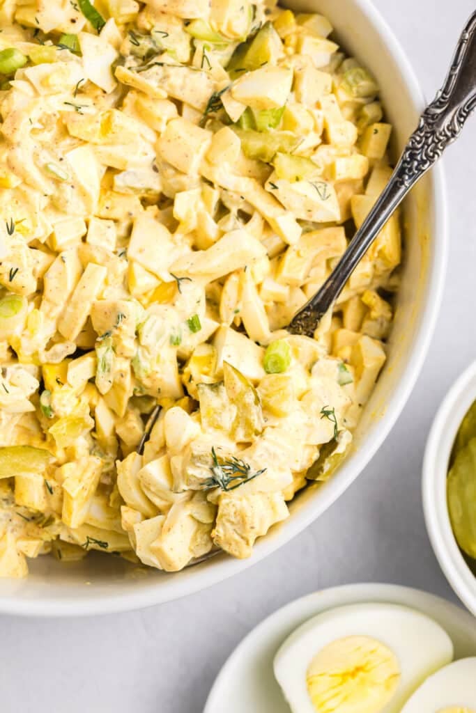 Close-up of a bowl of dill pickle egg salad with a spoon.
