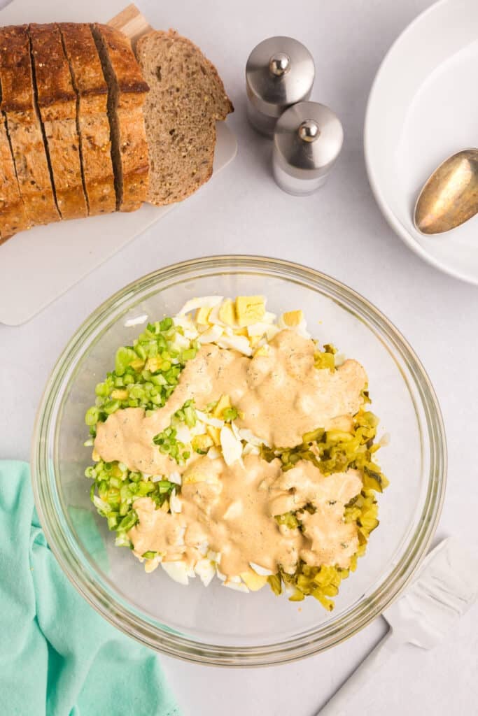 Unmixed dill pickle egg salad ingredients in a glass bowl.