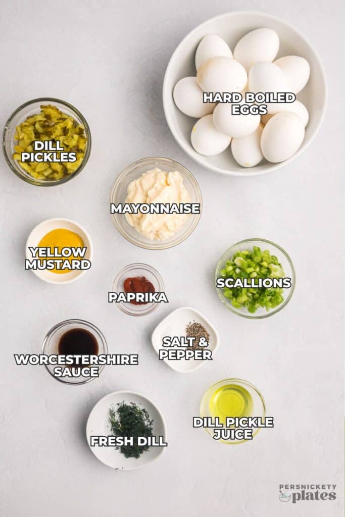 Labeled ingredients for dill pickle egg salad arranged on a light surface.