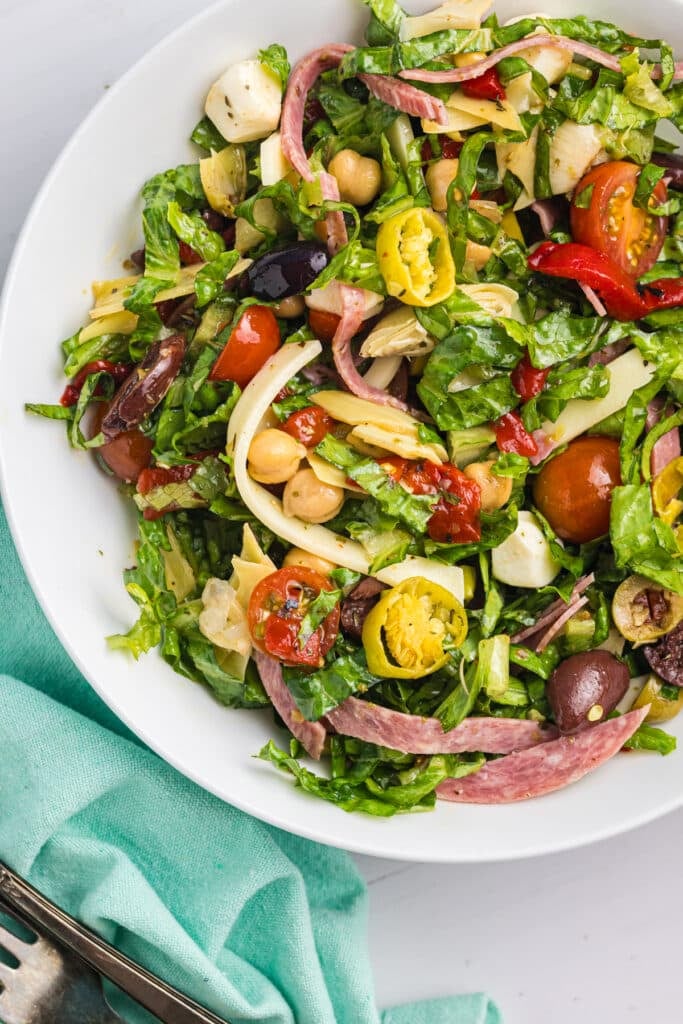 Antipasto salad in a white bowl with colorful toppings.