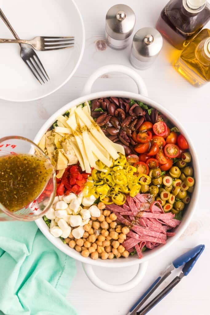 Dressing being poured over antipasto ingredients arranged in sections.