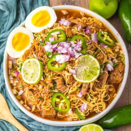 Close-up of birria ramen in a bowl with lime slices, soft eggs, and jalapeños.