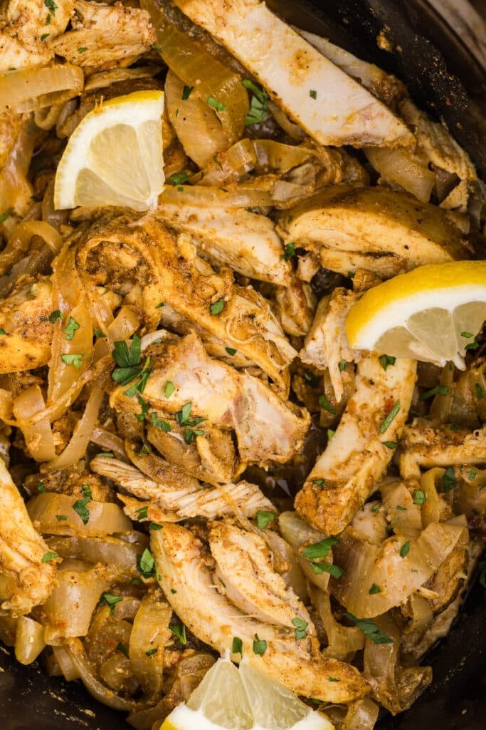 Close-up of cooked chicken shawarma with onions and lemon slices.