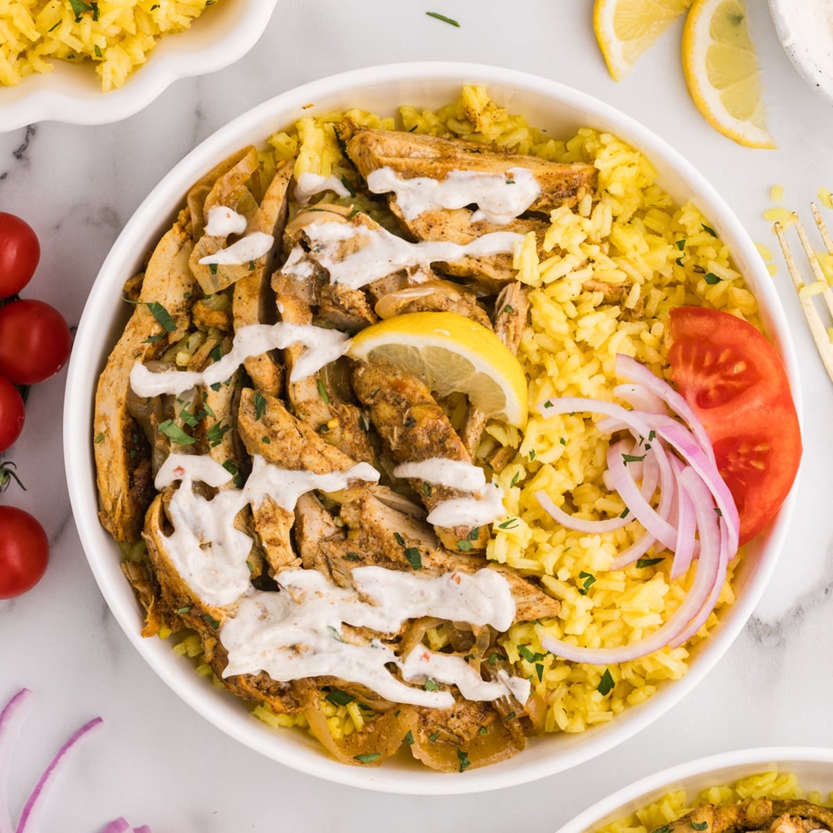 Bowl of yellow rice topped with sliced chicken shawarma, white sauce, and vegetables.