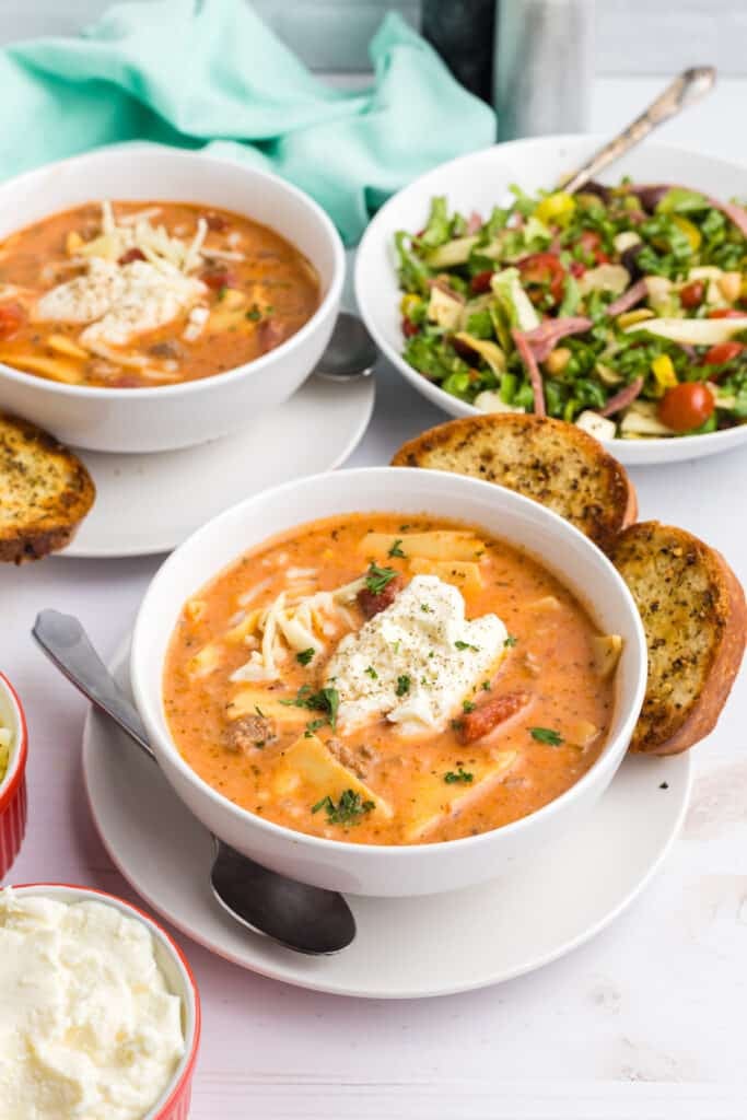 Two bowls of lasagna soup served with garlic bread and salad.