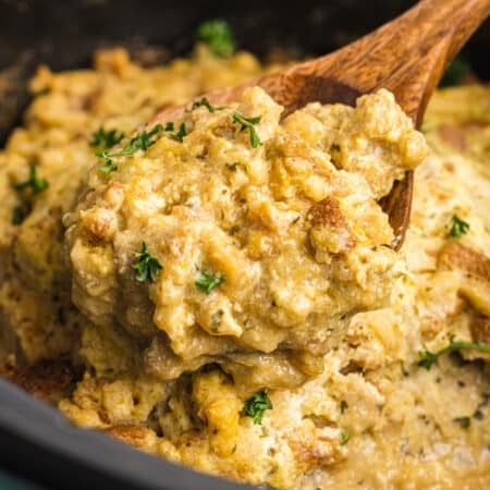 Spoonful of creamy stuffing casserole being lifted from a slow cooker.