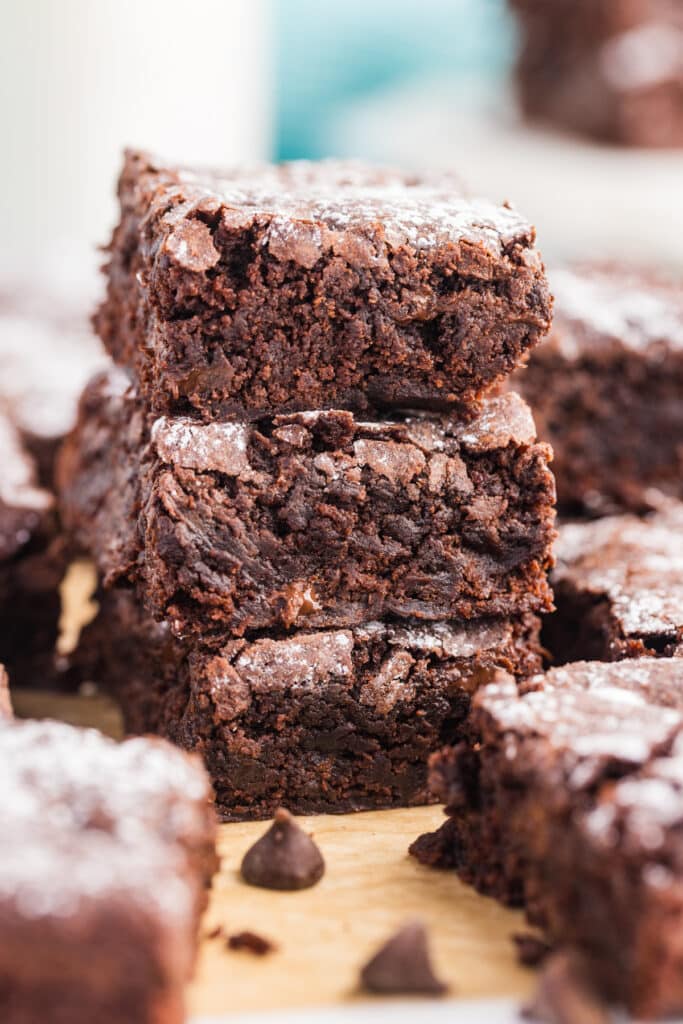 Three thick chocolate brownies stacked vertically, each with a crackly top and powdered sugar.