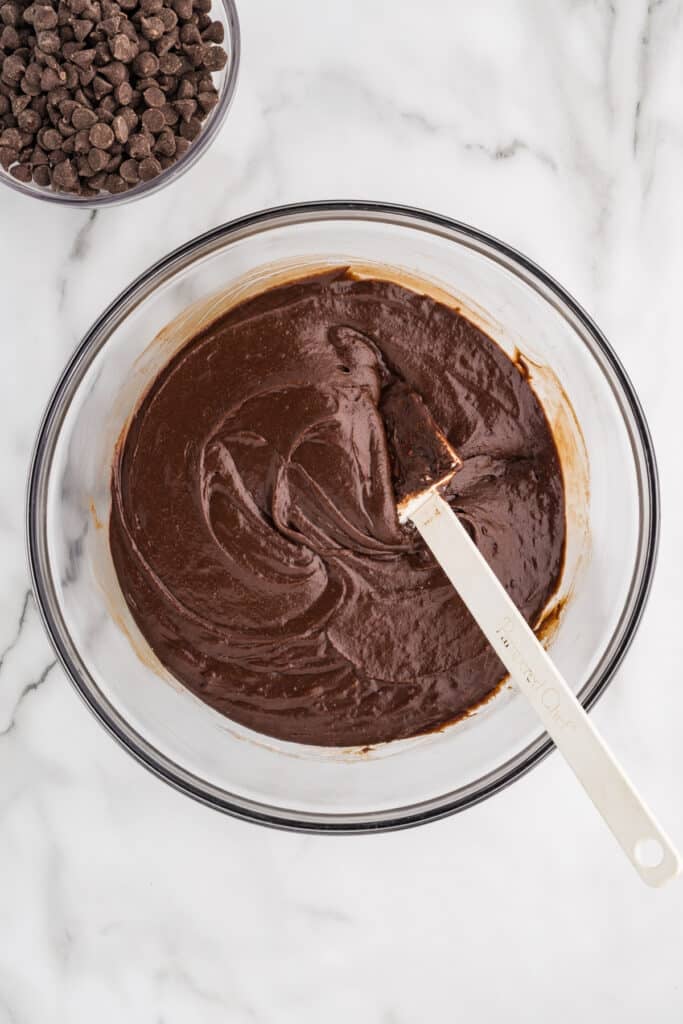 Chocolate brownie batter in a mixing bowl with a spatula.