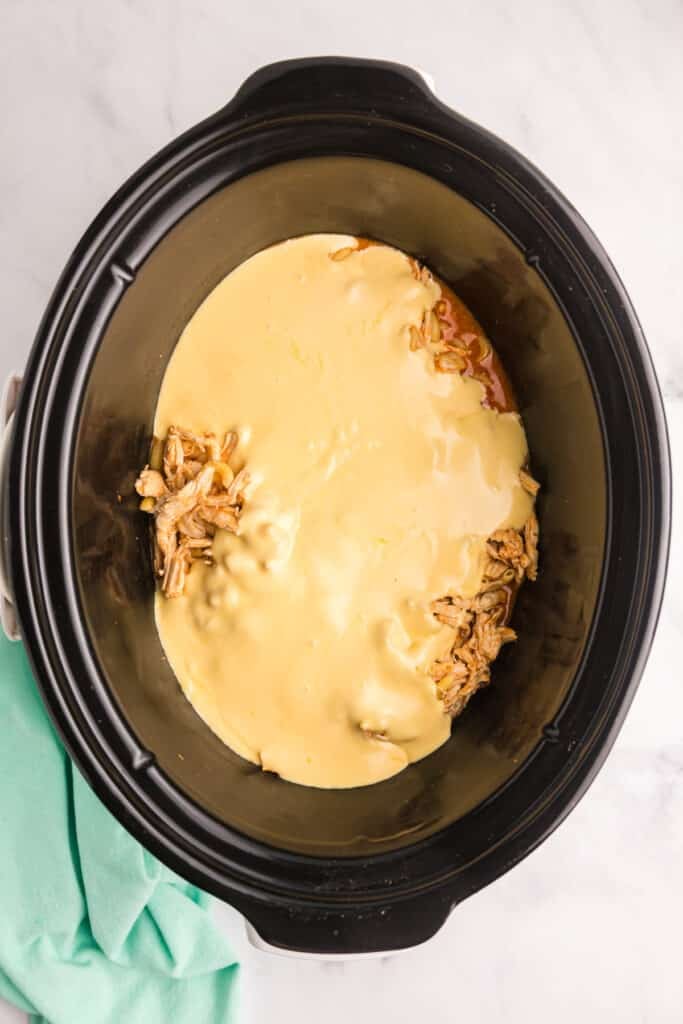 Melted cheese sauce poured over shredded chicken in a slow cooker.