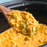 Wooden spoon lifting creamy buffalo chicken mac and cheese from slow cooker.